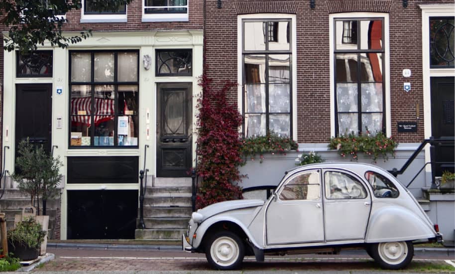 Weißer Oldtimer steht neben einem Grachtenhaus