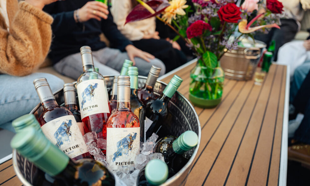 A bucket filled with bottles of wine on a wooden table. The wine bottles have white labels with a blue logo.