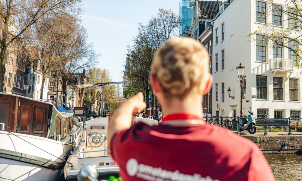 Tour guide pointing at a landmark in Amsterdam. A boat is moored along the canal.