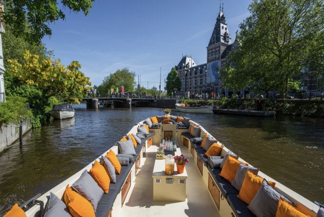 A boat with orange and grey seats on a canal. Amsterdam city trip.