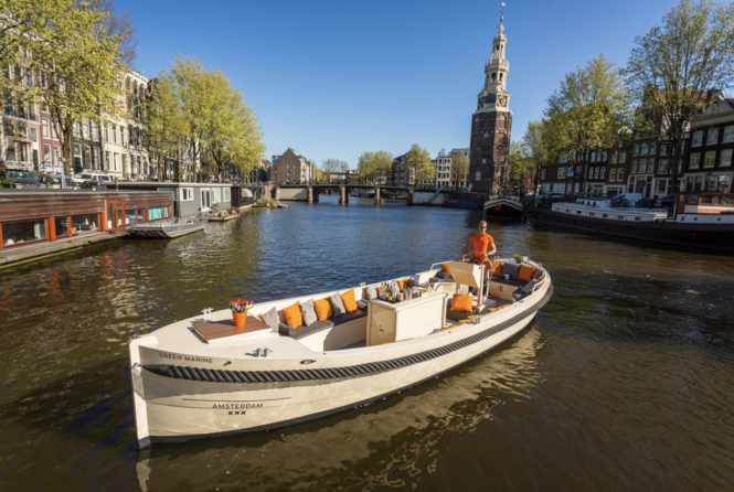 A white boat on a canal in Amsterdam. The boat is on a tour.