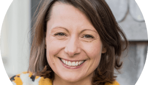 A smiling woman with brown hair and a yellow sweater.