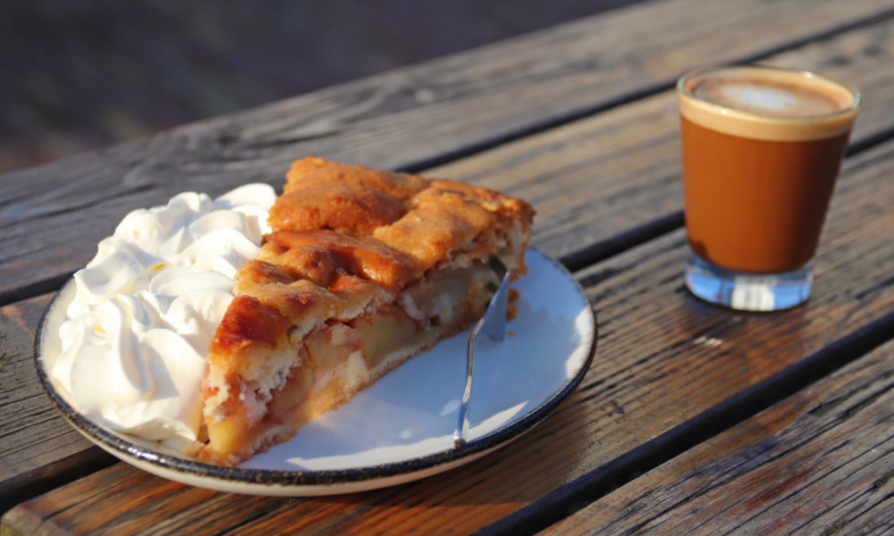 Apfelkuchen mit Sahne und einem Kaffee auf einem Holztische