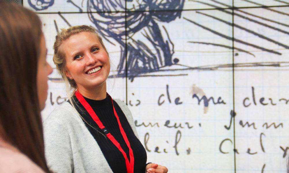 Woman smiling and looking at friend. Colourful wall in background.
