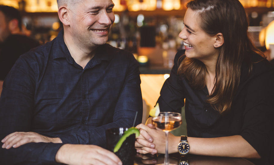 Ein lachendes Pärchen sitzt an der Bar und trinken Cocktails