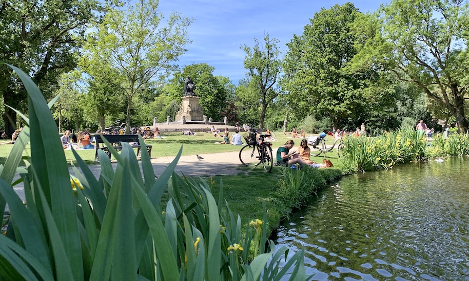 Besucher sitzen im grünen Vondelpark neben Bäumen und Teich