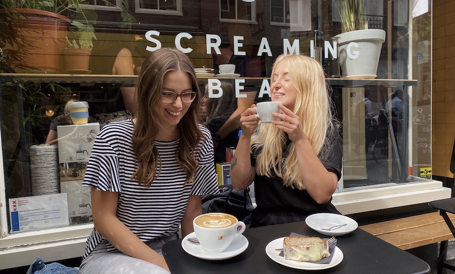 Two smiling women sit outside the Streaming Beans Café with a coffee