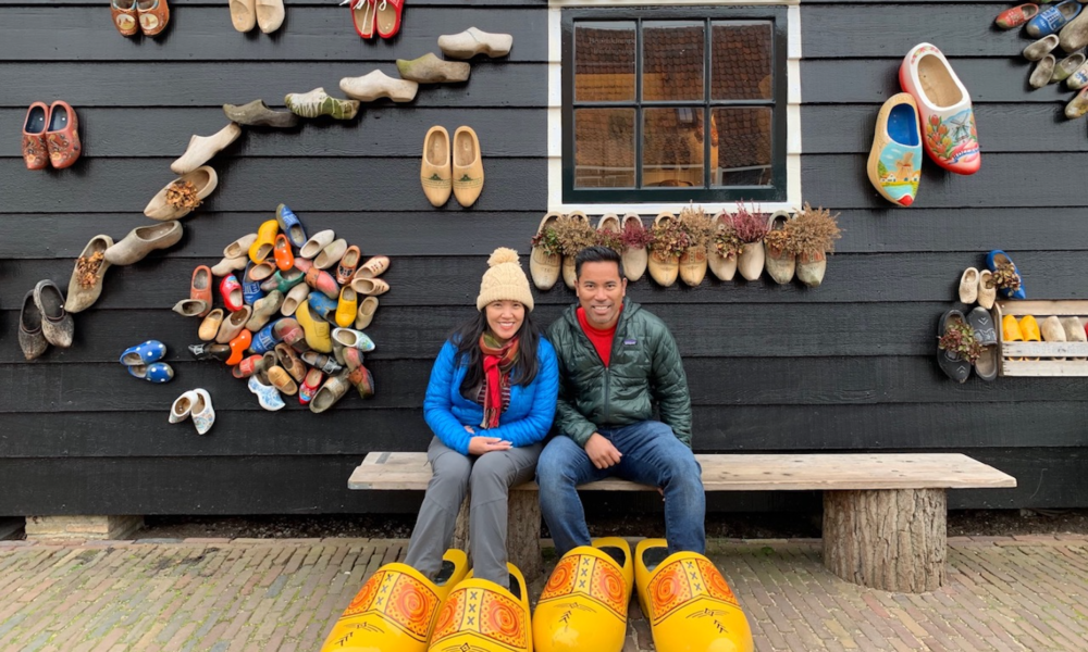 Amsterdamliebe Tourteilnehmer sitzen vor einer Holzschuhmanufaktur und haben übergroße Holzschuhe an