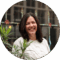 A smiling woman with dark hair standing in front of green plants. She appears to be on a city trip in Amsterdam.