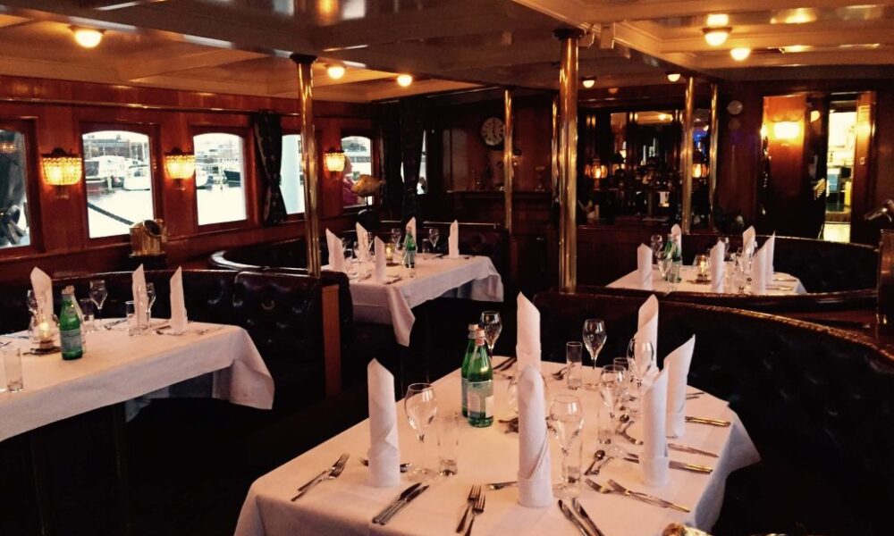 Elegant dining room on a canal boat in Amsterdam. Tables set for dinner with white linens and glassware.