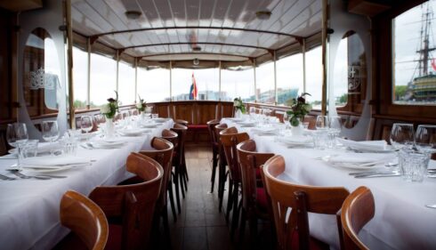 Elegant dining area on a boat with white tablecloths and wooden chairs. A perfect setting for a city trip to Amsterdam.