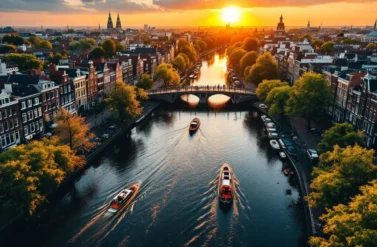Aerial view of Amsterdam's UNESCO canal ring with colorful Dutch houses, boats, and bridges at golden hour sunset.