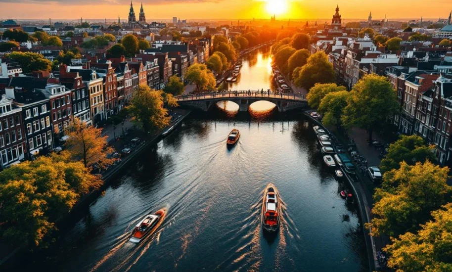 Aerial view of Amsterdam's UNESCO canal ring with colorful Dutch houses, boats, and bridges at golden hour sunset.