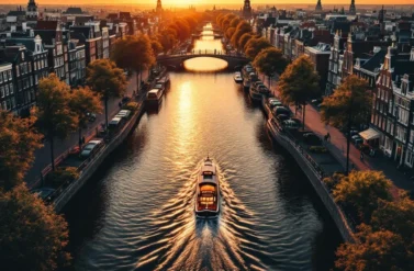 A boat on a canal in Amsterdam during sunset. The cityscape and trees are reflected in the water.