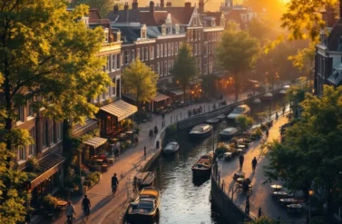 A serene canal in Amsterdam lined with boats and cafes. People stroll along the sidewalk enjoying the scenery.
