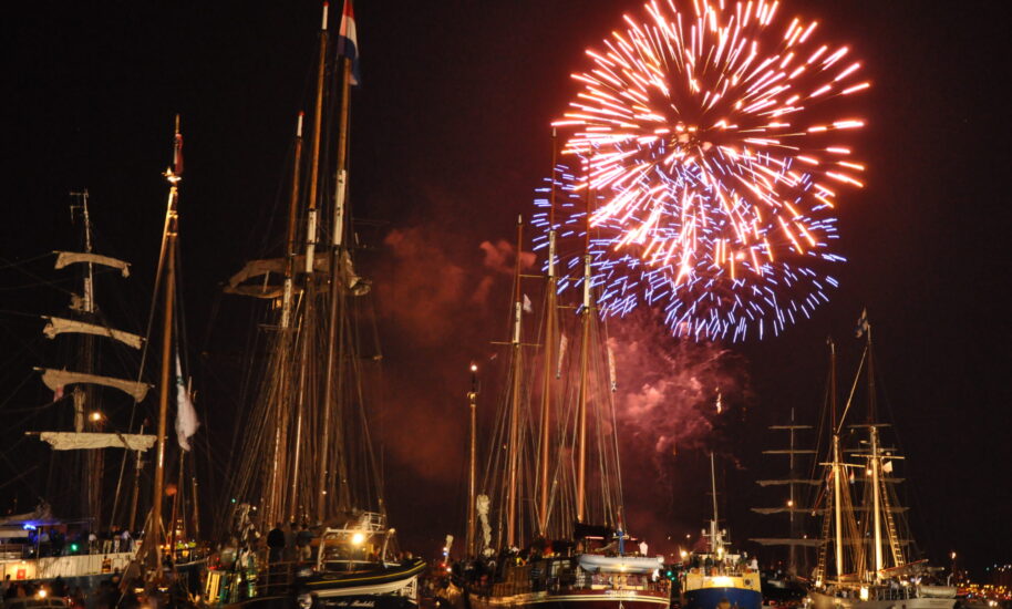 Fireworks explode over a harbour in Amsterdam at night. Many boats are moored in the harbour.