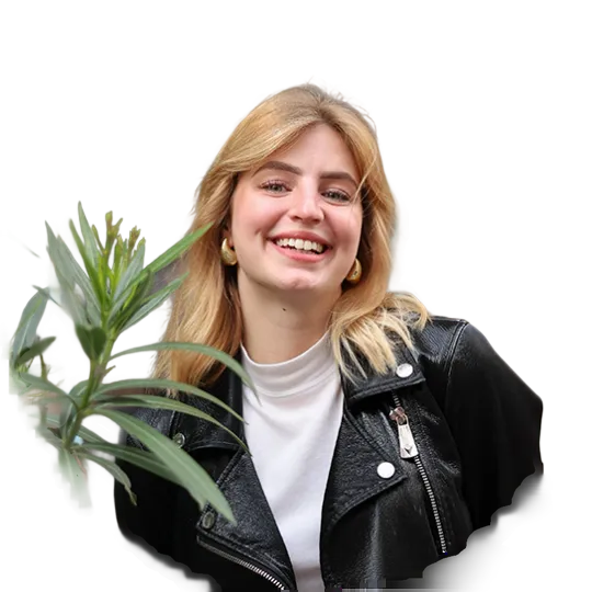 Smiling blonde woman wearing a leather jacket. She is standing next to a plant.