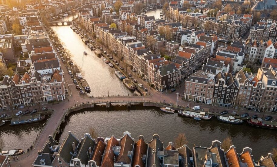 Aerial view of Amsterdam's UNESCO World Heritage canal rings with historic Dutch houses, bridges, and boats in golden sunlight