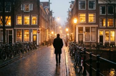 Person walking confidently down illuminated Amsterdam canal street at night with historic buildings and glowing windows.