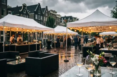 Elegant white corporate event tents on wet Amsterdam cobblestones with Dutch canal houses and dramatic overcast sky