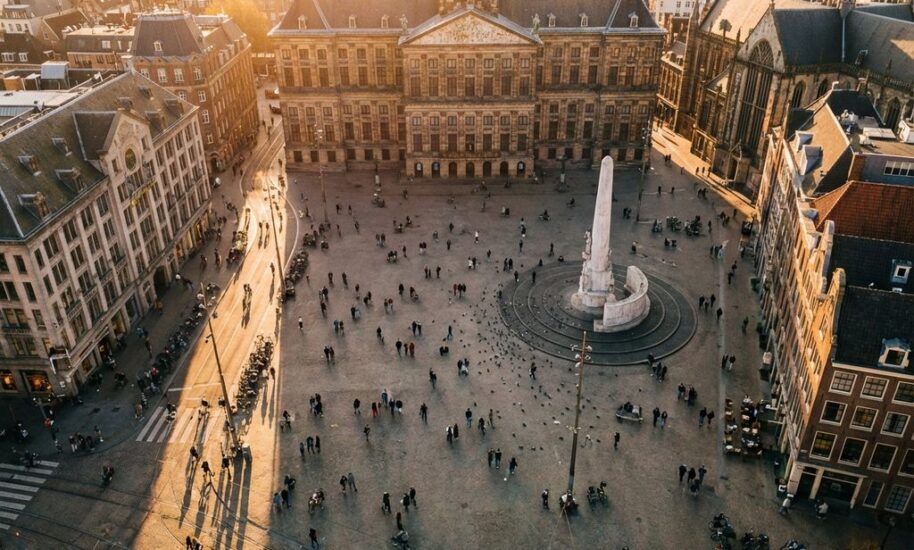 Amsterdam's Dam Square at golden hour with Royal Palace, National Monument, tourists on cobblestones, and traditional Dutch buildings