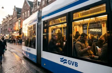 Amsterdam tram with passengers traveling through city center past Dutch canal houses during golden hour sunset