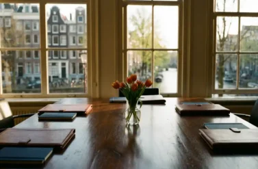 Conference table with leather portfolios and tulip centerpiece overlooking Amsterdam canal houses through large windows