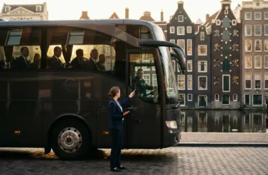 Professional woman with tablet coordinating with bus driver beside modern coach bus parked on Amsterdam canal street