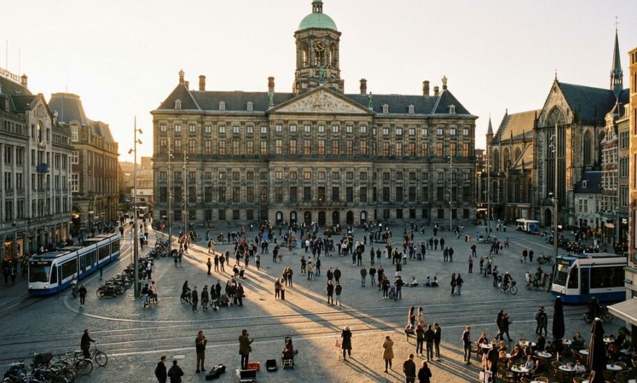 Dam Square in Amsterdam with Royal Palace's neoclassical facade, tourists walking on cobblestones, and golden afternoon light.