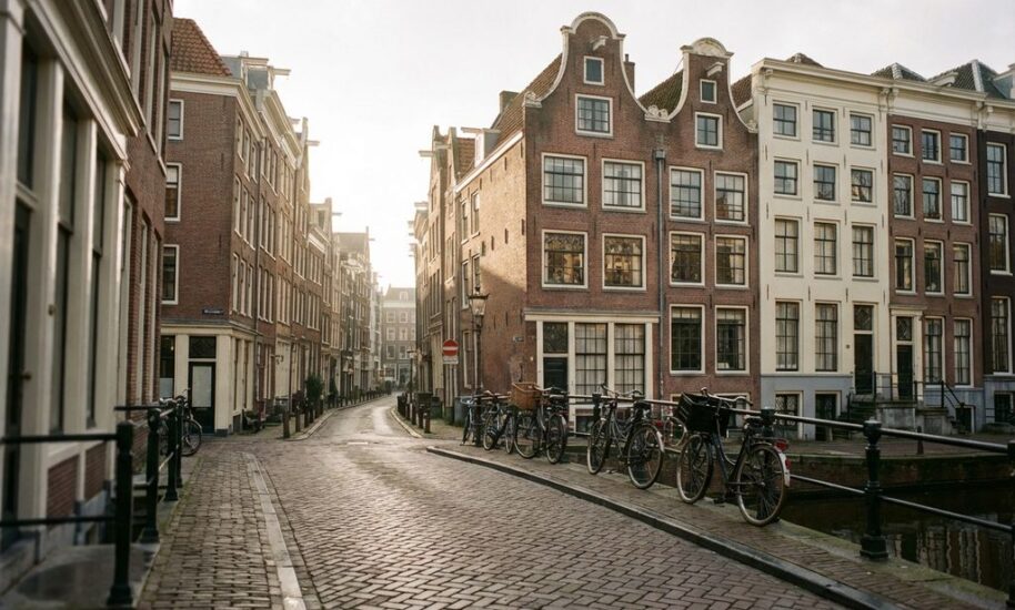 Historic Dutch canal houses with traditional gabled roofs line cobblestone street, bicycles parked beside peaceful canal
