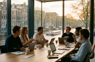 Diverse startup professionals collaborating around wooden table in Amsterdam conference room with canal houses visible through windows