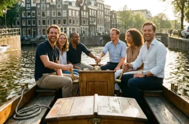 Diverse team of professionals laughing together on canal boat in Amsterdam with historic Dutch gabled houses