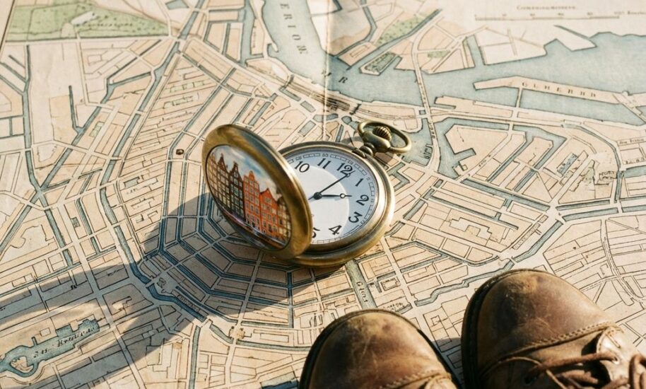 Vintage pocket watch showing 2:30 on Amsterdam canal map with Dutch houses reflected in watch face, leather shoes nearby