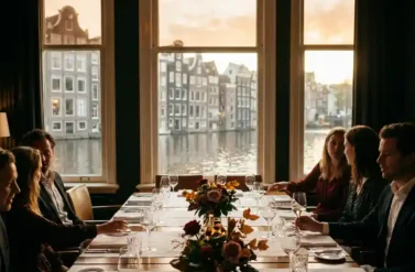 Elegant dining table for eight with white linens and crystal glasses overlooking Amsterdam's historic canal ring through tall windows