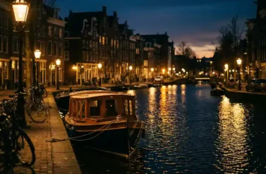 Amsterdam canal at twilight with historic gabled houses reflecting in water, golden streetlights, and moored Dutch boat