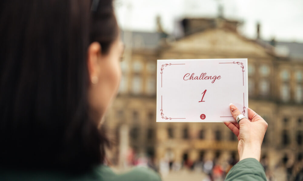 A woman holding a white card with a challenge written on it. The card reads 'Challenge 1'.