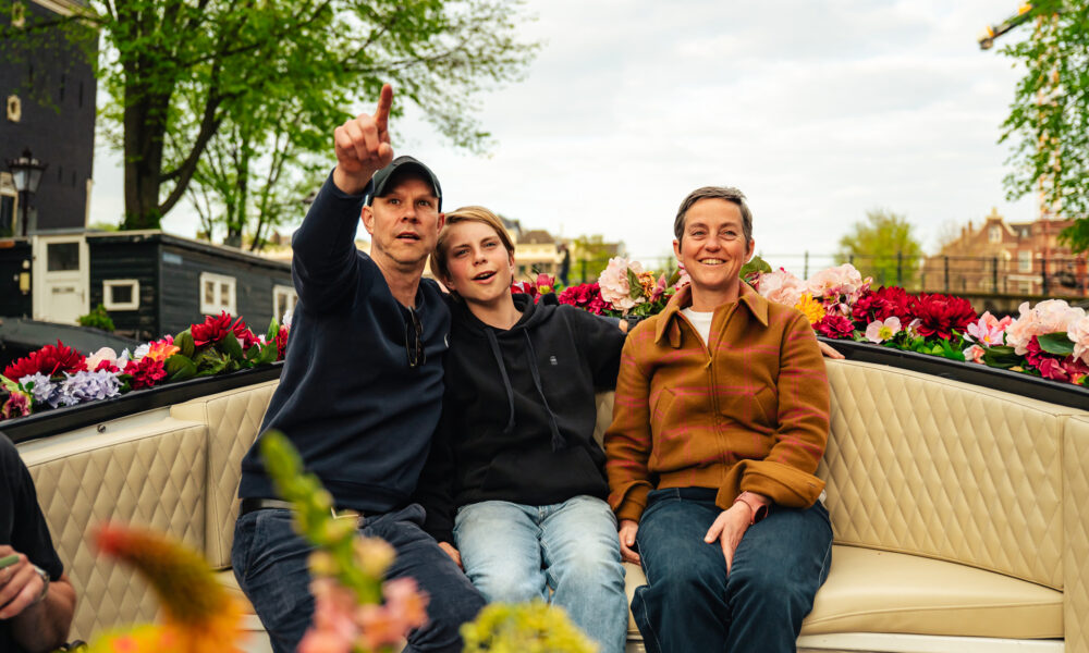 Three friends smiling and enjoying a boat tour. Colorful flowers in the background.